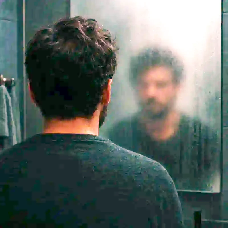 The back of a man's head reflected in a fogged bathroom mirror