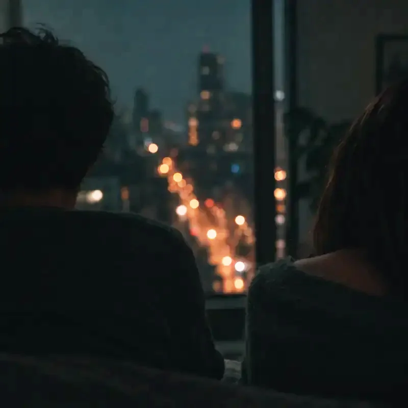 Two people's shoulders at a night window, city lights beyond