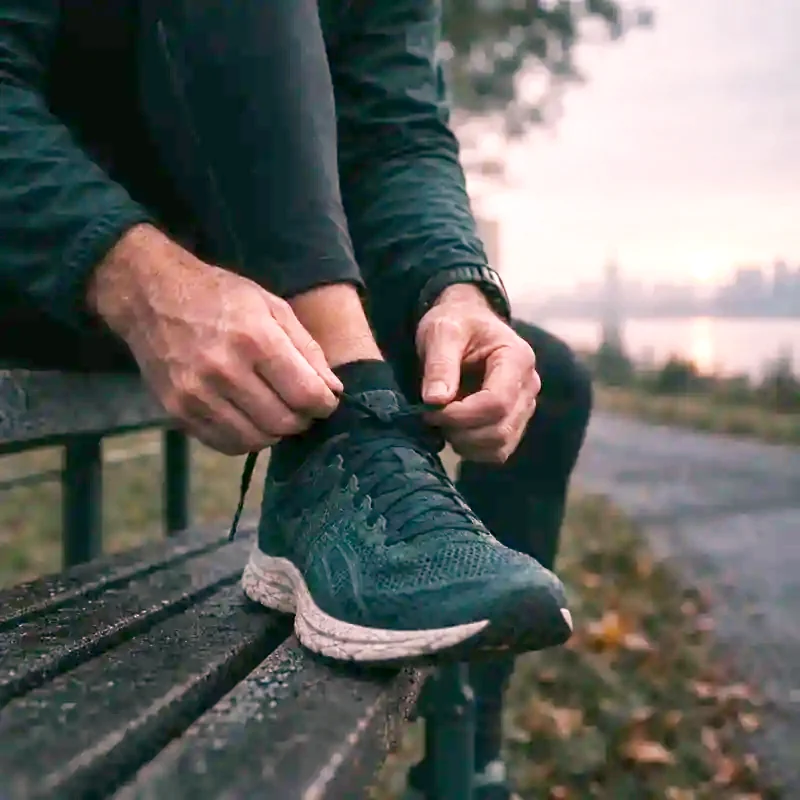 Hands lacing a running shoe on a bench at dawn